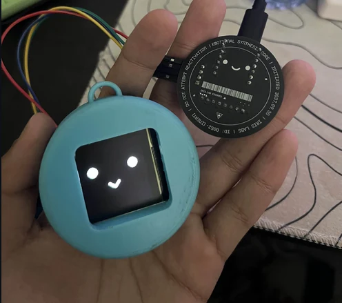 A hand holding the working blue HackCharm OLED companion alongside its circular PCB